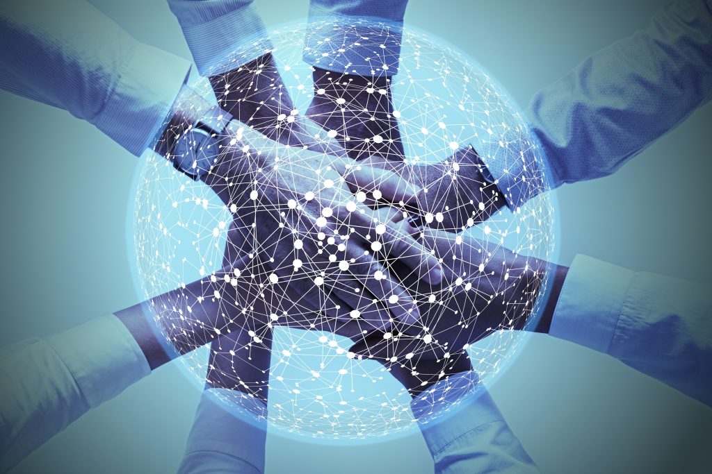 Image of a bunch of hands layered on top of each other in a circle for a team, with an image of connected dots in a circle over the top of the hands. Image is meant to show AI and human power combining together. 