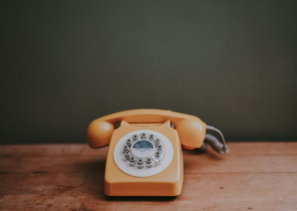 an orange rotary phone sits on a wooden desktop